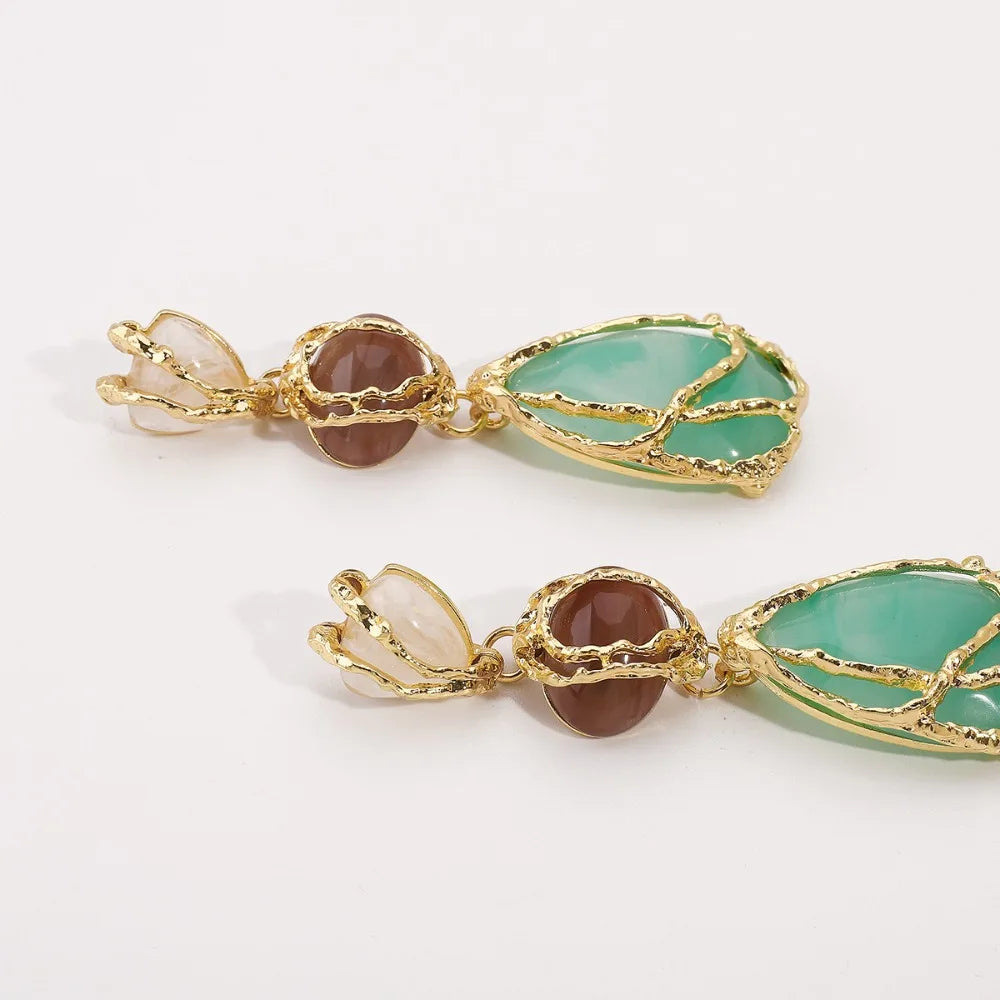 Pair of gold earrings with green and brown gemstones on a white background