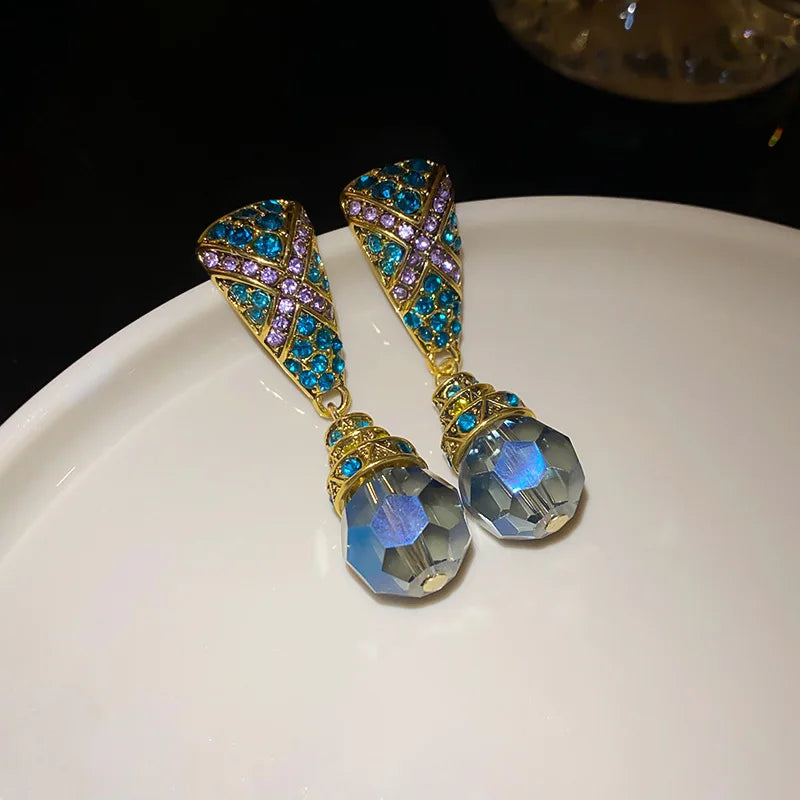 Pair of ornate earrings with blue and purple gemstones on a white surface.