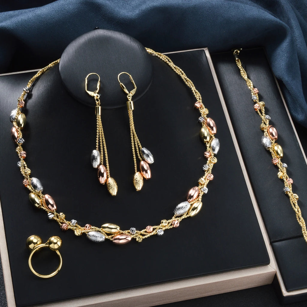 Gold jewelry set including necklace, earrings, ring, and bracelet on a dark surface.