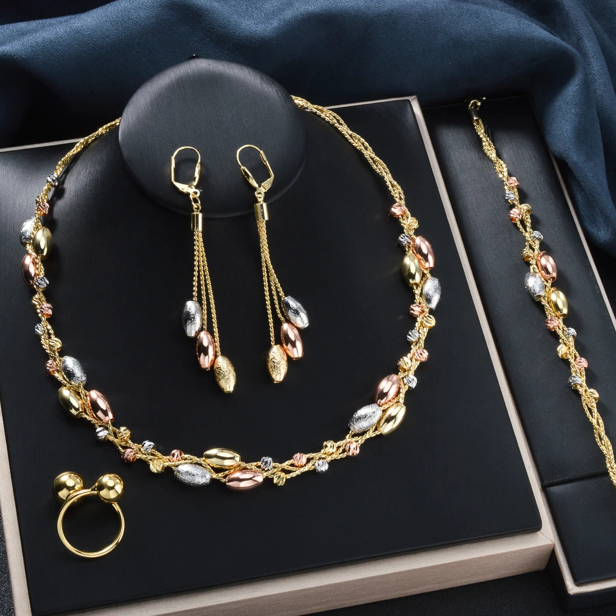 Gold jewelry set including necklace, earrings, ring, and bracelet on a dark surface.