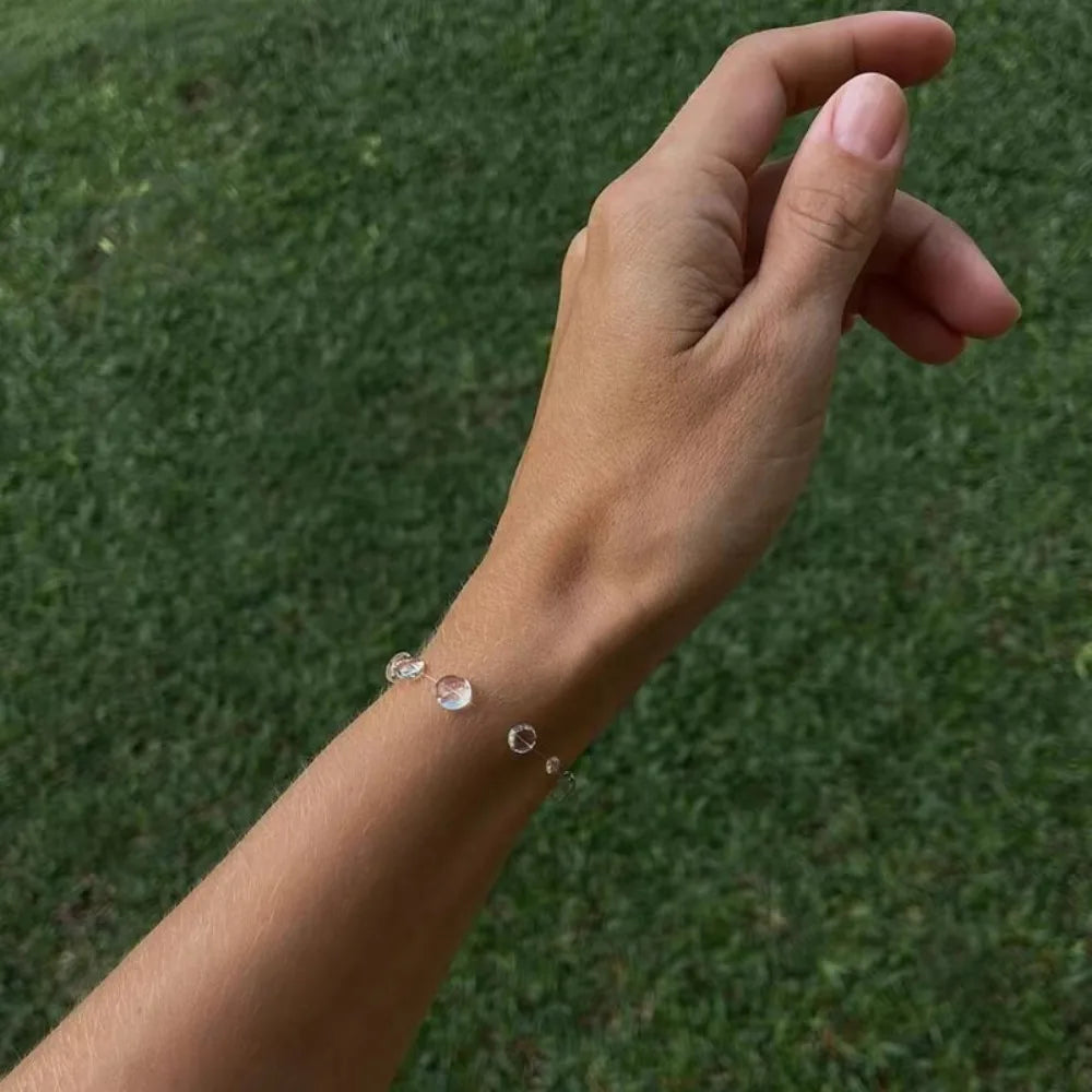 Hand wearing a bracelet with clear stones against a grass background