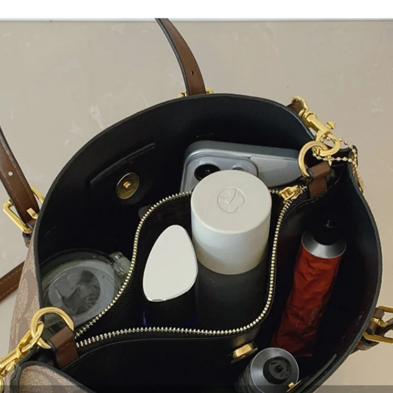 Open handbag with personal items including a phone, bottle, and container on a neutral background