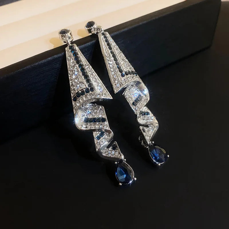 Pair of silver earrings with blue gemstones on a dark surface