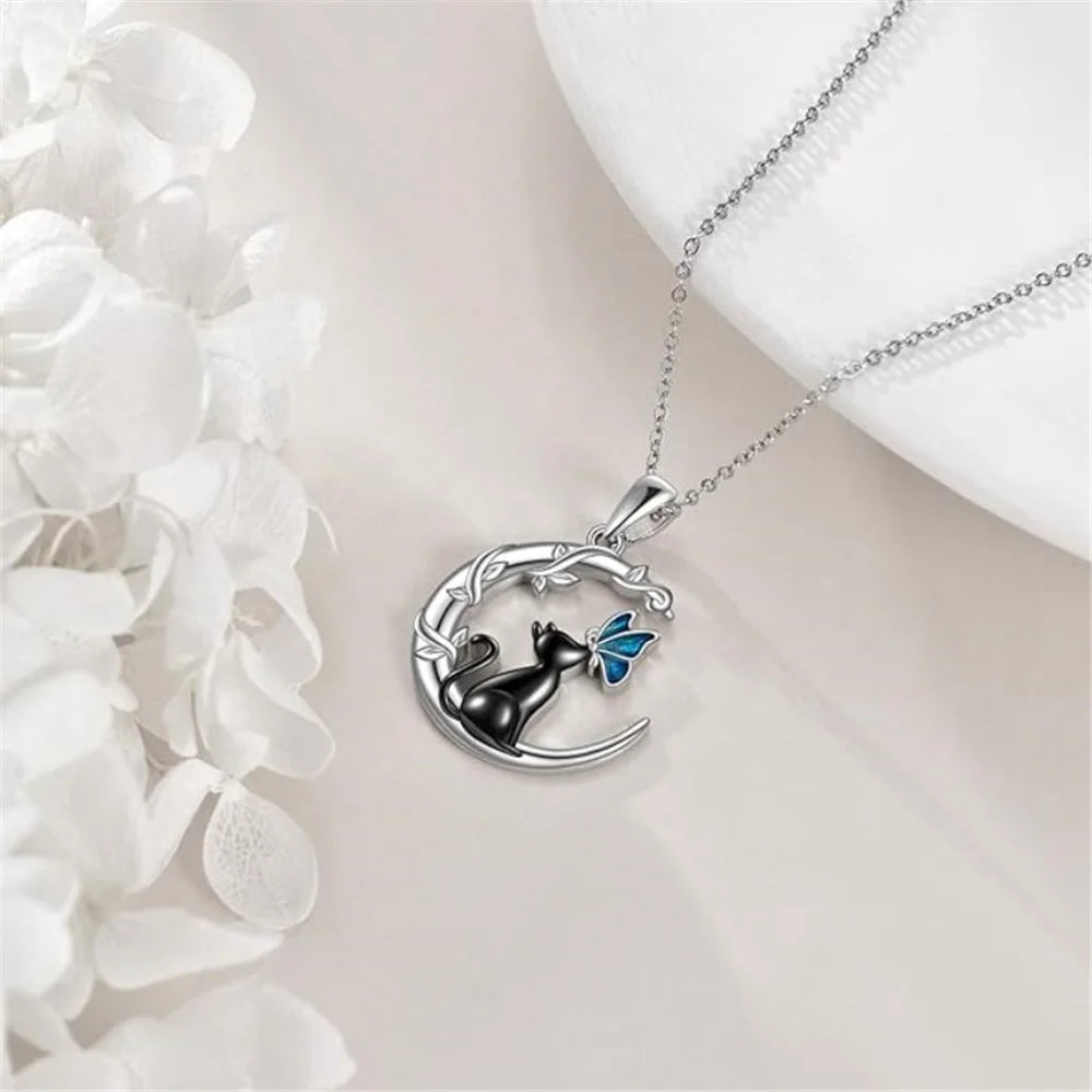 Silver necklace with a black cat and blue butterfly pendant on a white surface.