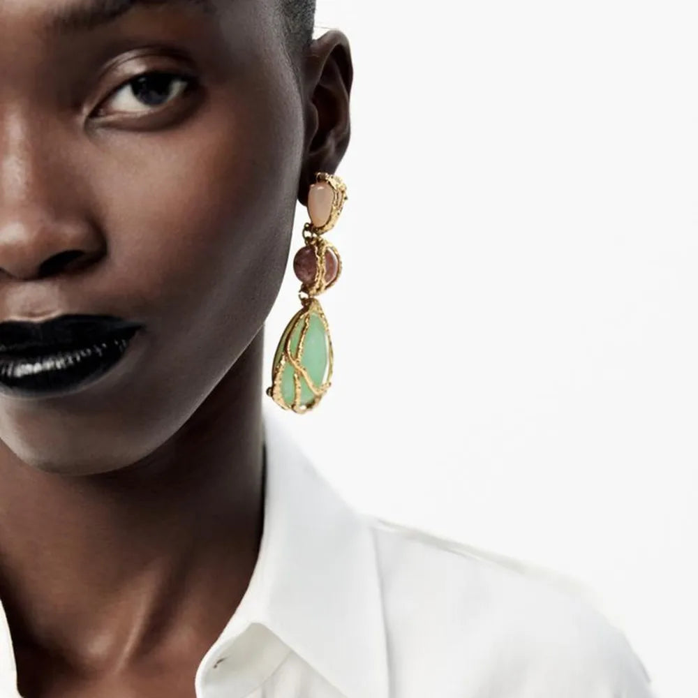 Close-up of a person wearing gold earrings with green stones on a white background