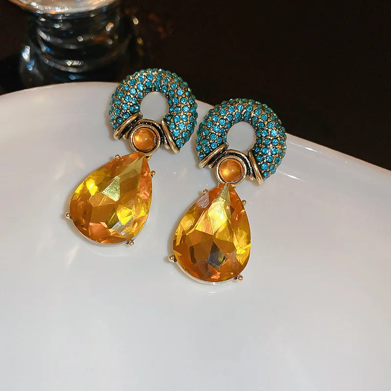 Pair of earrings with yellow teardrop stones and blue accents on a white plate.