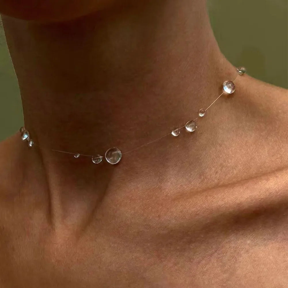 Necklace with clear beads on a person's neck against a neutral background