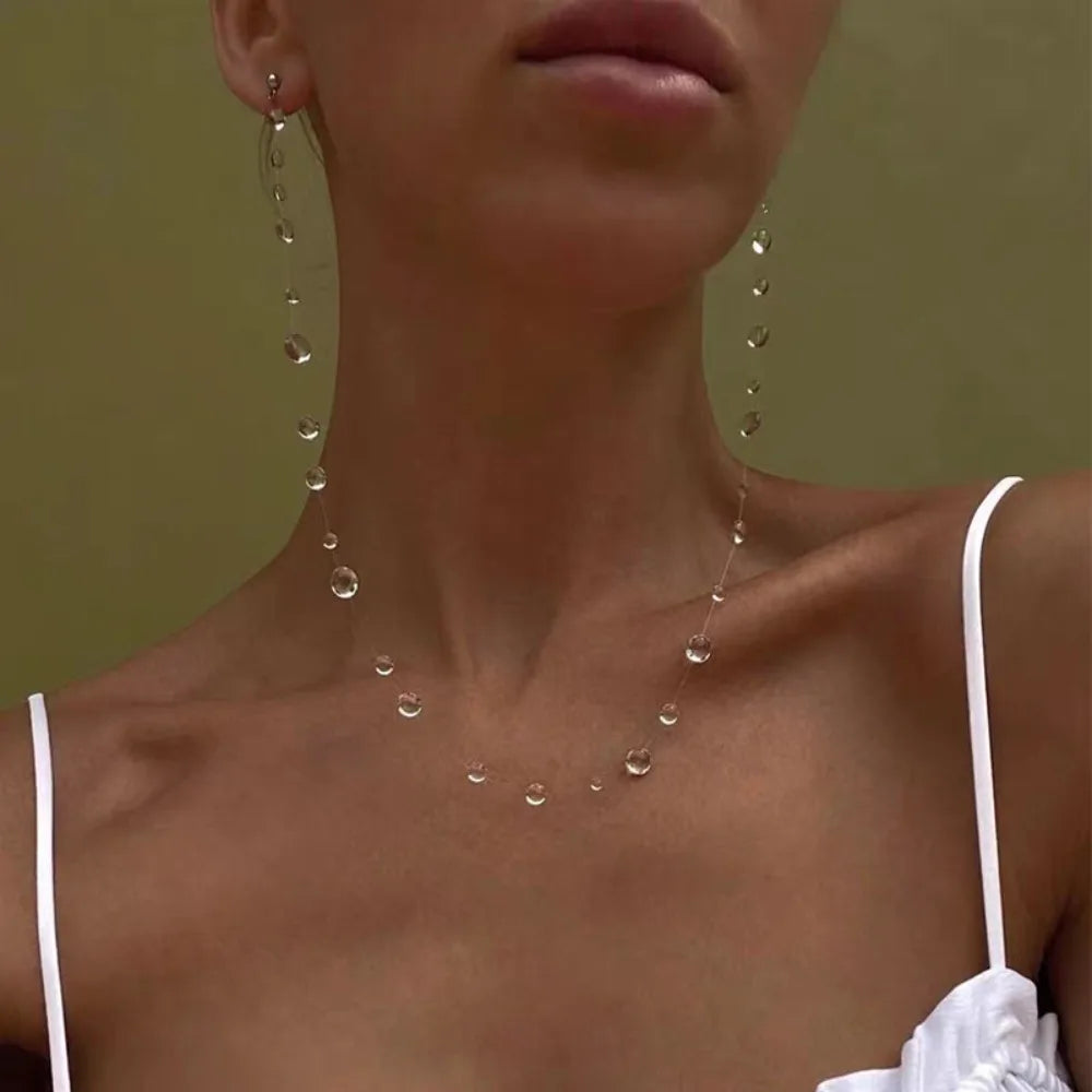 Close-up of a woman wearing a delicate necklace with dangling beads against a neutral background.