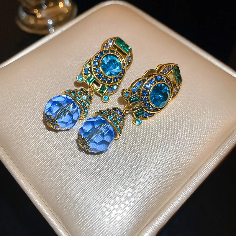 Pair of gold earrings with blue and green gemstones on a beige surface.