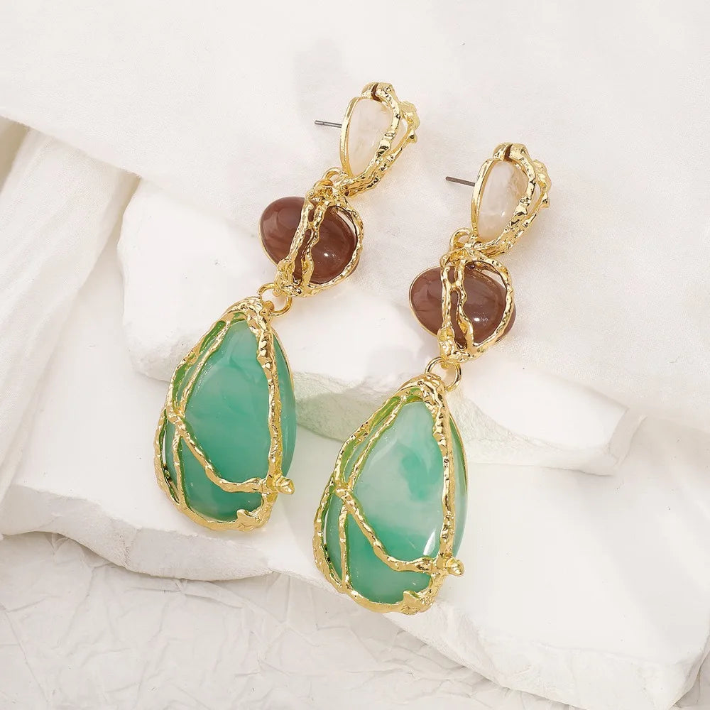 Gold earrings with green teardrop-shaped stones on a white fabric background