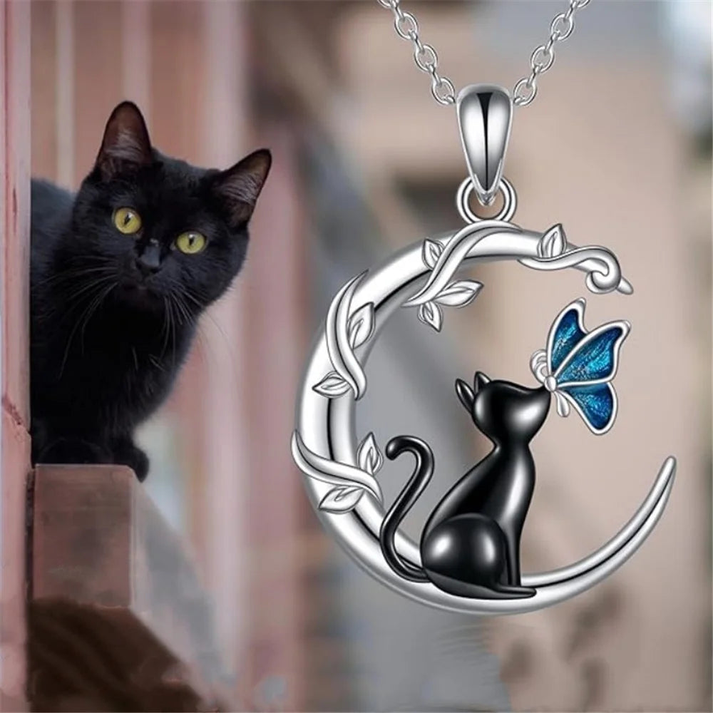Silver necklace with a cat and butterfly design next to a black cat.