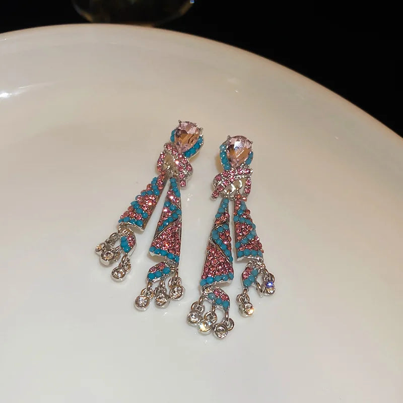 Pair of decorative earrings with pink and blue patterns on a white surface.