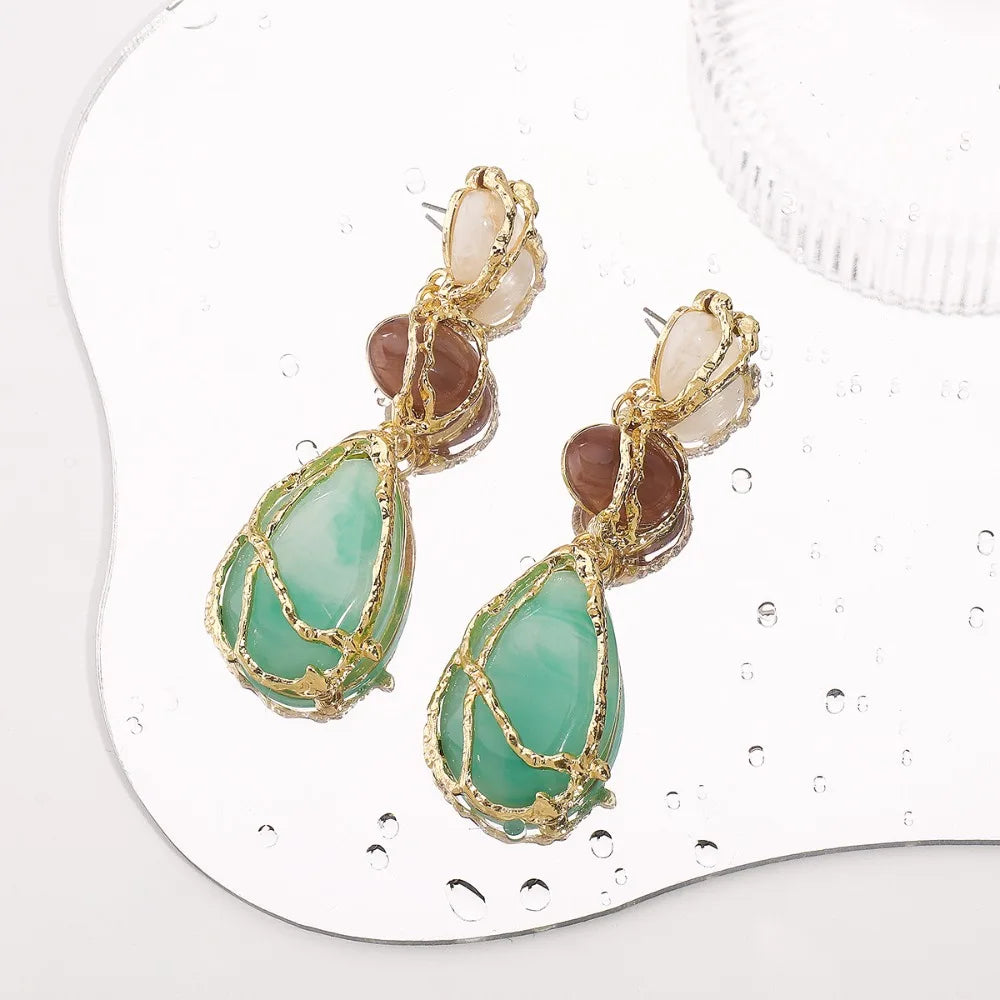 Gold-framed earrings with green and brown stones on a white background