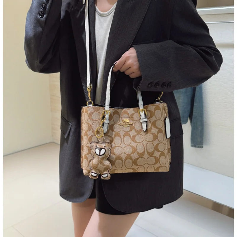 Person holding a Coach handbag with a teddy bear charm in an indoor setting