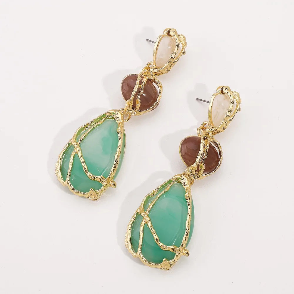 Pair of earrings with gold frames and green stones on a white background