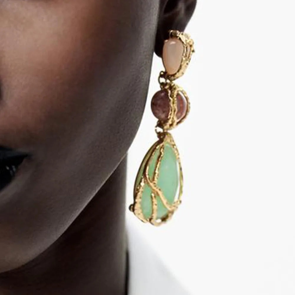 Close-up of an earring with green and pink stones on a neutral background