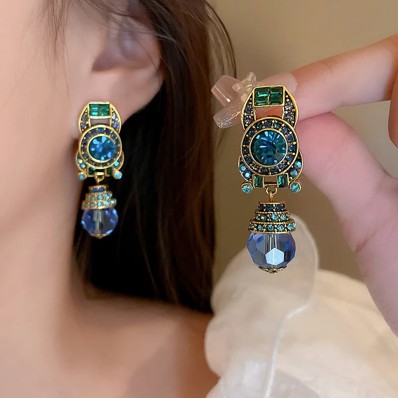 Earrings with blue and green gemstones held up to an ear.