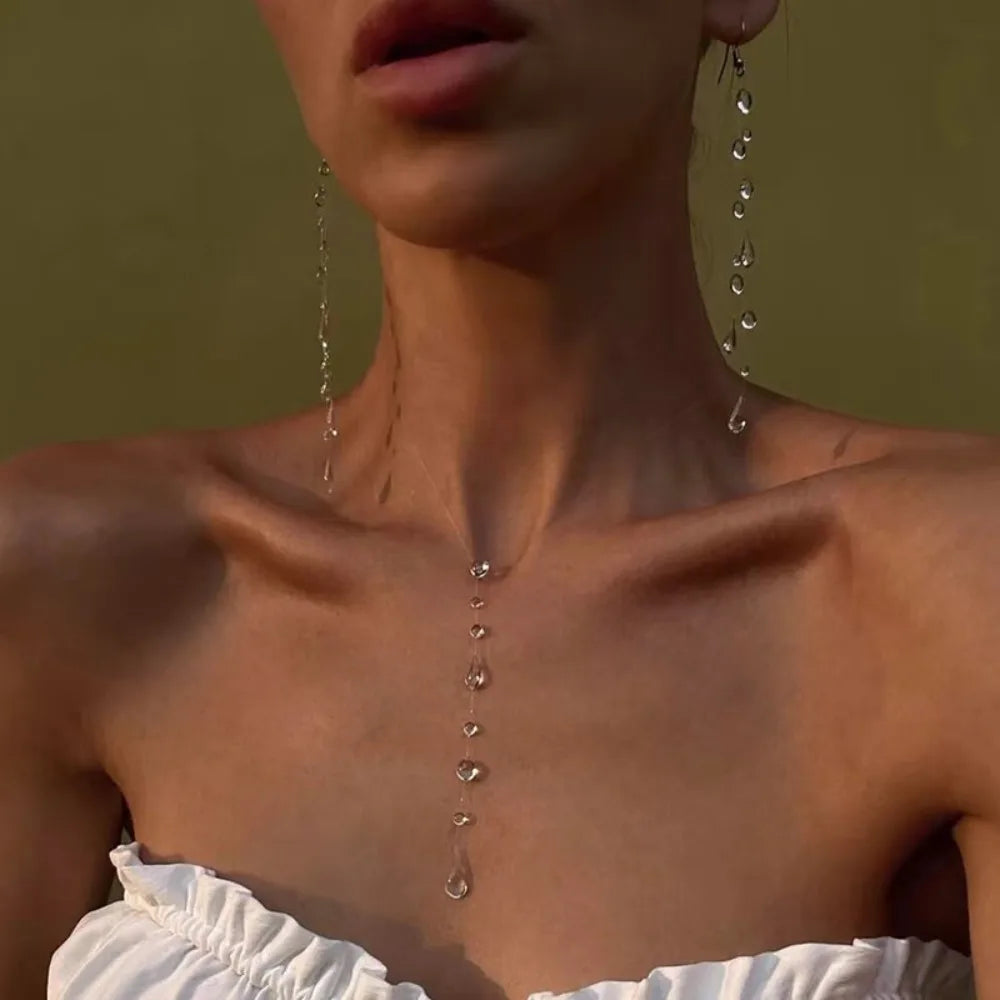 Close-up of a person wearing long, dangling earrings with a neutral background